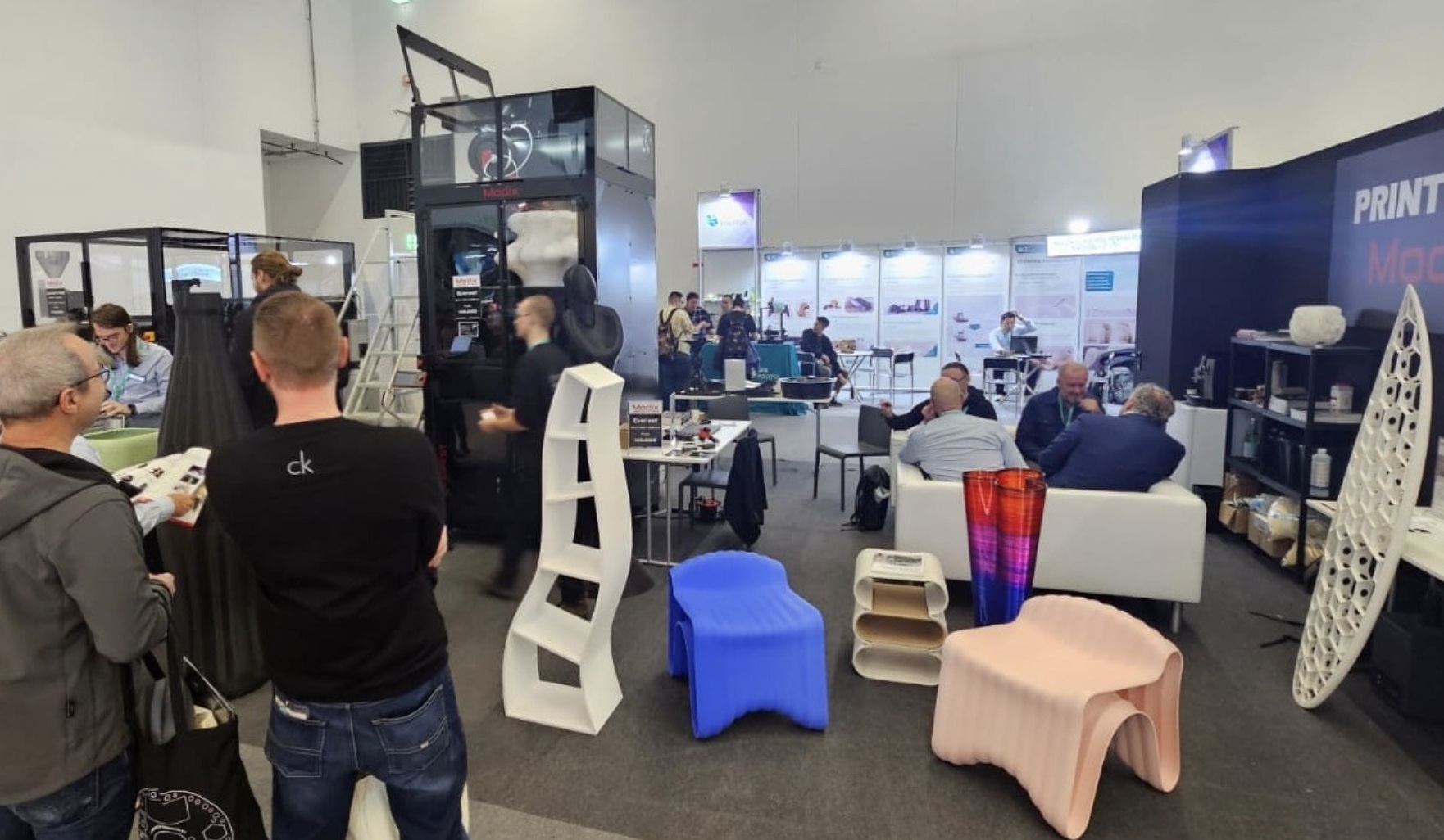 Visitors and printed parts at a Modix trade show booth